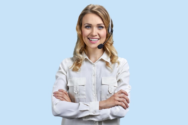 Happy call center operator with headset crossing arms on blue background