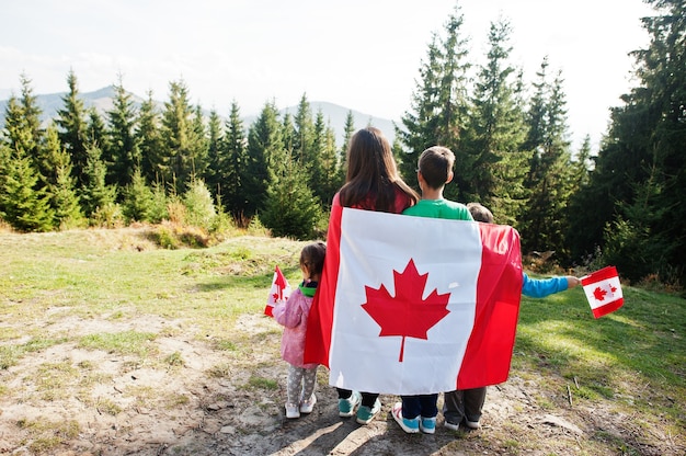 Happy Canada Day. Family of mother with three kids hold large Canadian flag celebration in mountains.