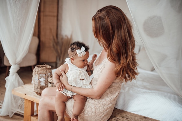 Happy candid authentic mother holding mixed race baby daughter in your arms at cozy apartment