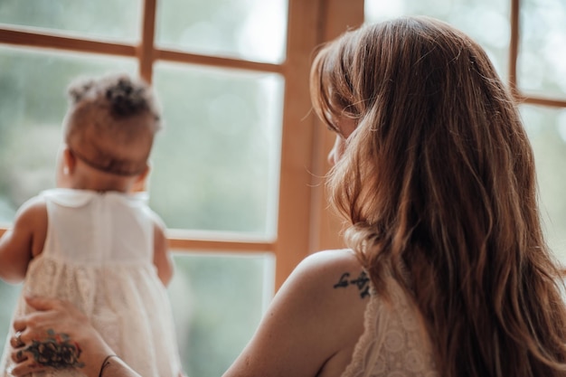 Happy candid authentic mother holding mixed race baby daughter in your arms near window