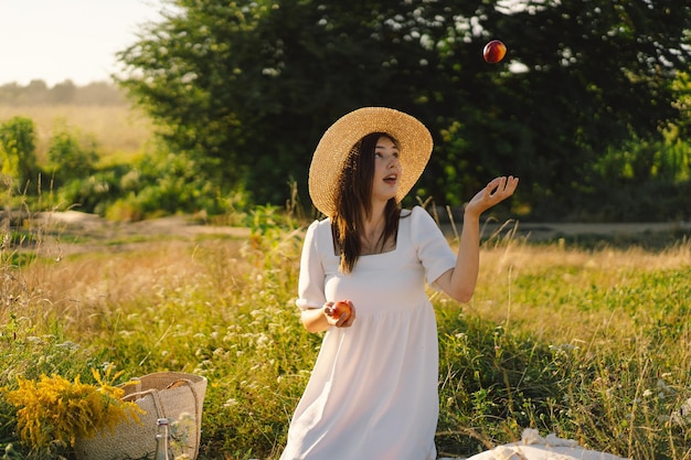 Happy carefree summer girl in outdoor field with orange peach fruit Young woman eats peach Summer picnic setting