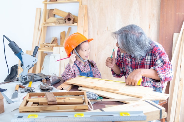 Happy carpenter family. The little girl and her grandfather raising your hands while working on woodwork in a wooden shop.