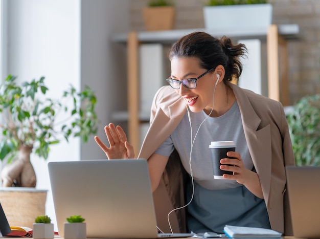 Happy casual beautiful woman working on a laptop, talking with somebody in office.