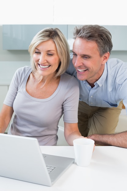 Happy casual couple using laptop in kitchen