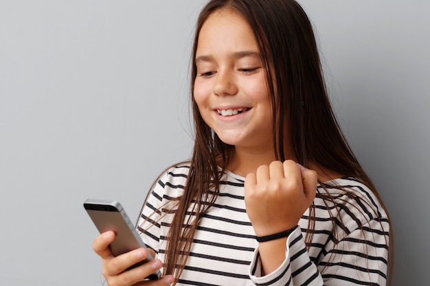 Happy casual little girl looking at her phone over gray background