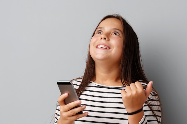 Happy casual little girl looking at her phone over gray background