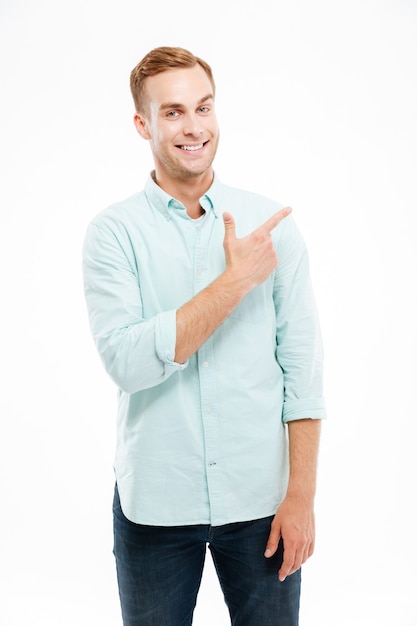 Happy casual man pointing finger away at copyspace isolated on a white wall