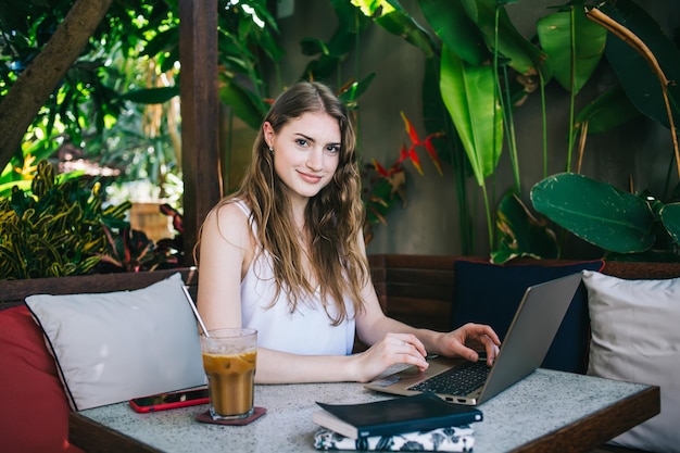 Happy casual woman using laptop while sitting on tropical terrace