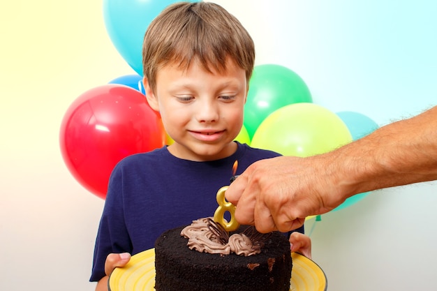 Happy caucasian boy celebrates birthday by holding a chocolate cake