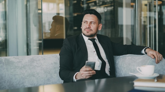 Happy Caucasian businessman in formal clothes smiling and holding his smartphone