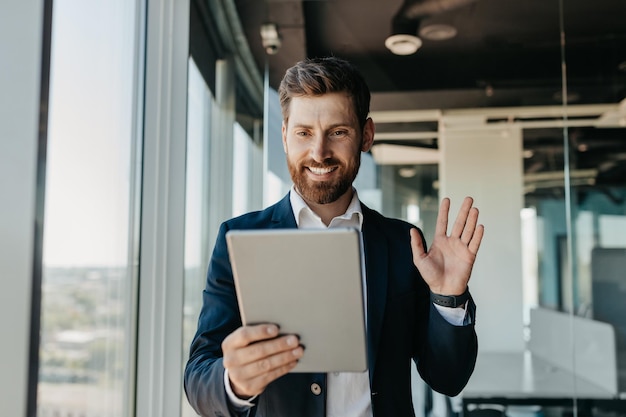 Happy caucasian businessman in suit working in office having video chat with business partners via digital tablet