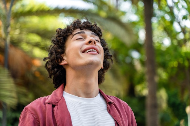 Happy caucasian curly man relaxing with closed eyes while standing at the street