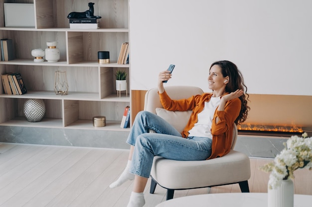 Happy caucasian girl has video phone call at home in weekend morning Young woman is using airpods