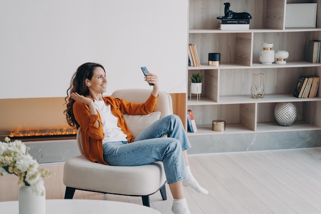 Happy caucasian girl has video phone call at home in weekend morning Young woman is using airpods