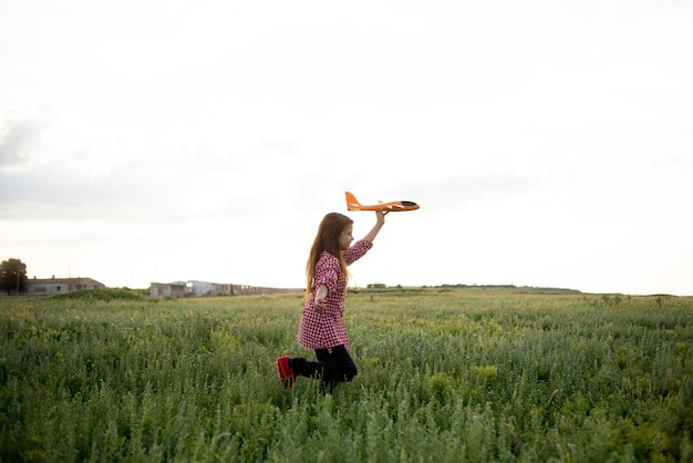 Happy Caucasian girl running across the field launches a toy airplane into the sky with her hand up joyful child walks alone runs on the grass