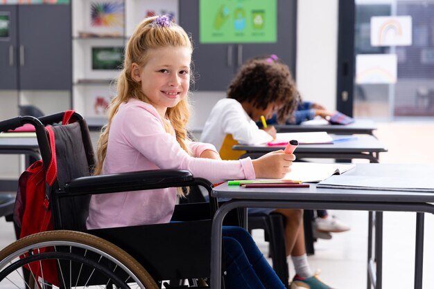 Happy caucasian girl in wheelchair with diverse children in classroom