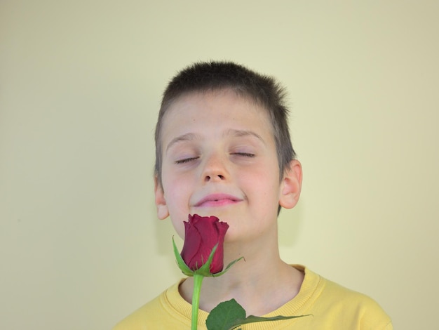 Happy caucasian kid smelling the red rose witch eye closed