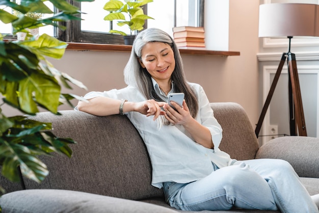 Happy caucasian mature woman using smart phone on the sofa in the living room