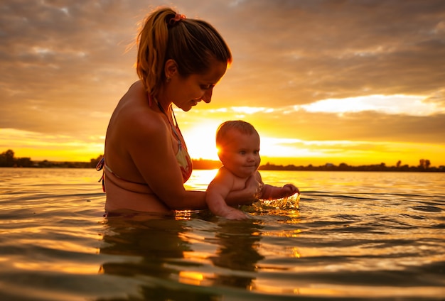 Happy caucasian mother swimming with little cute smiling baby in sea