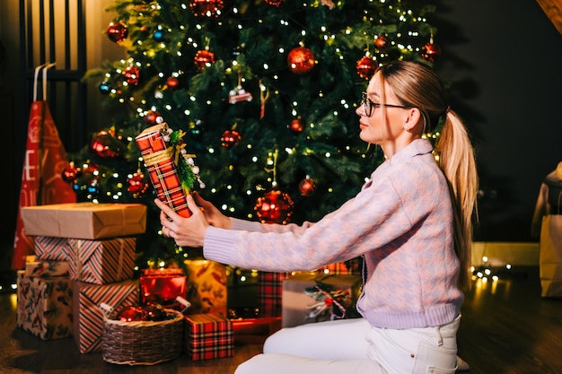 Happy caucasian woman holding big Christmas present near Christmas tree.