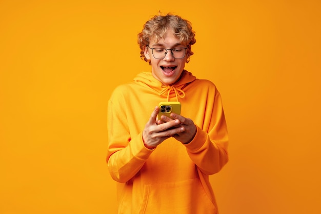 Happy caucasian young man using smartphone against yellow background