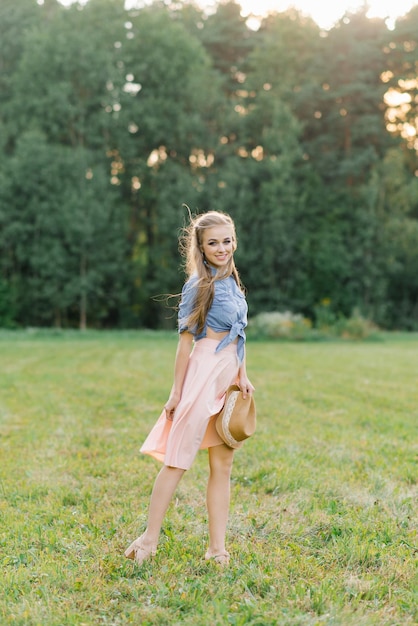 Happy Caucasian young woman girl walking in the summer outdoors in nature holding a hat in her hands