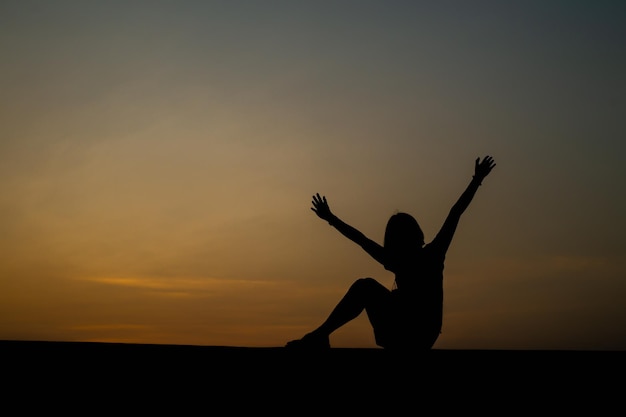 Happy celebrating winning success woman at sunset or sunrise standing elated with arms raised up above her head