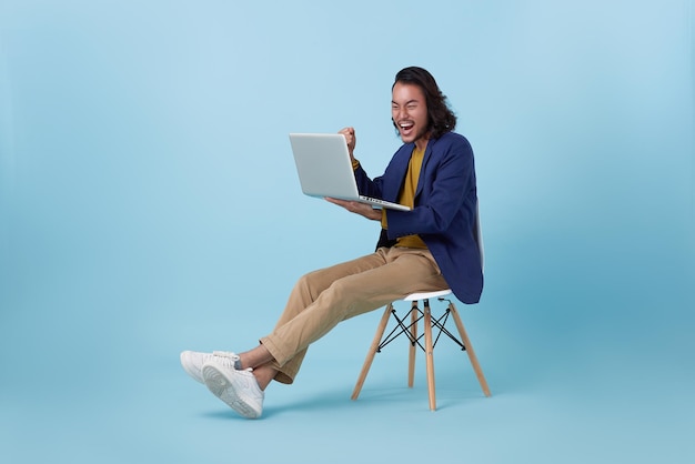 Happy celebration asian business man achievement goal using computer laptop sitting on white chair