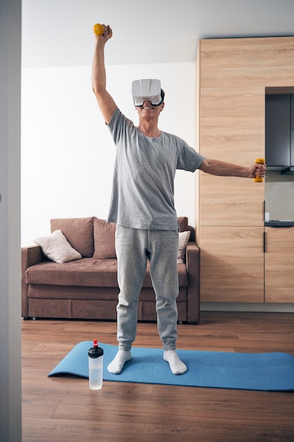 Happy cheerful adult male person standing on yoga mat while doing morning exercise in room