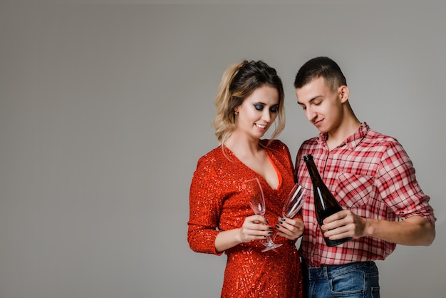 Happy cheerful couple celebrating holding glasses with champagne and petards over gray