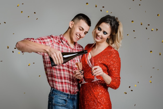 Happy cheerful couple celebrating new year holding glasses with champagne over gray