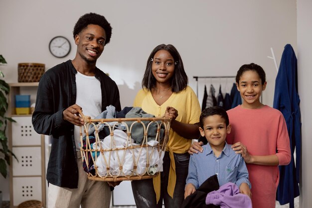 The happy cheerful family does household chores together in the laundry room Parents hold a large wicker basket with clothes to sort young children daughter son help learn to clean