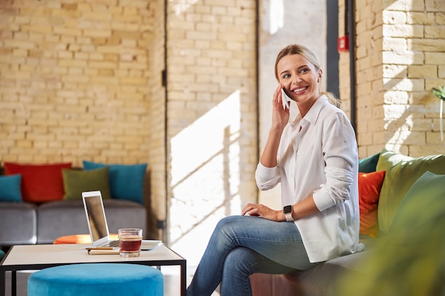 Happy cheerful lady in white blouses talking on mobile phone in the indoors