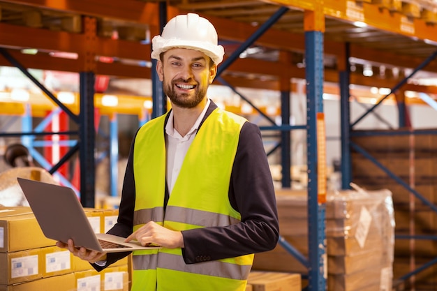 Happy cheerful man looking at you while organizing the logistics system of the warehouse