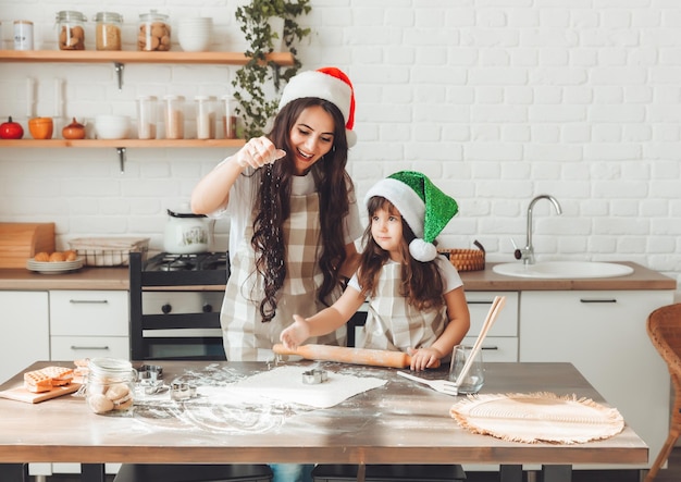 Happy cheerful mother and child in Santa Claus hats are cooking Christmas cookies in the kitchen new year and Christmas