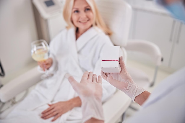 Happy cheerful patient with glass of water looking to her doctor in beauty center