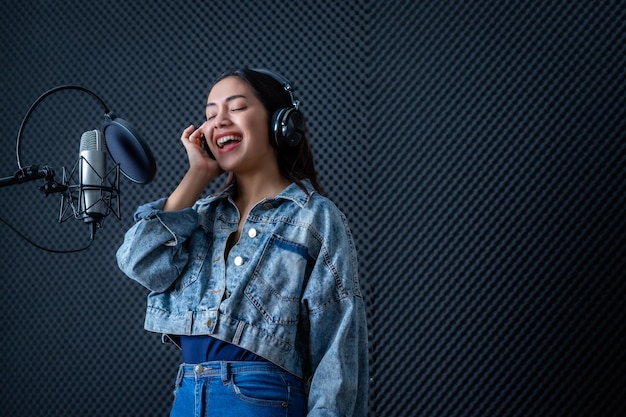 Happy cheerful pretty smiling of portrait of young Asian woman vocalist Wearing Headphones recording a song front of microphone in a professional studio