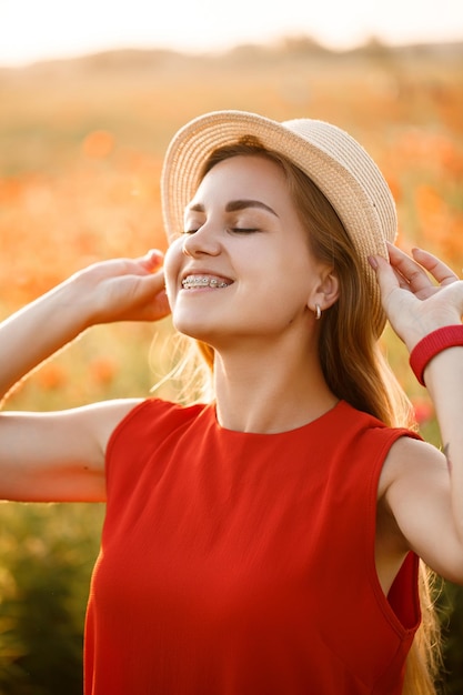 Happy cheerful woman walking on blooming field poppies. Red flowers. A blonde in a red short dress and a hat.