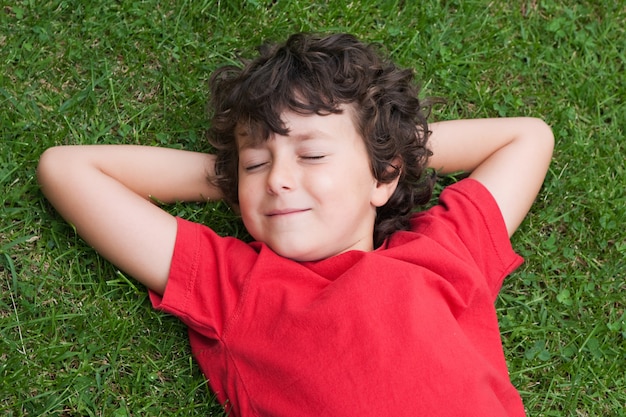 Happy child asleep on the grass with red shirt