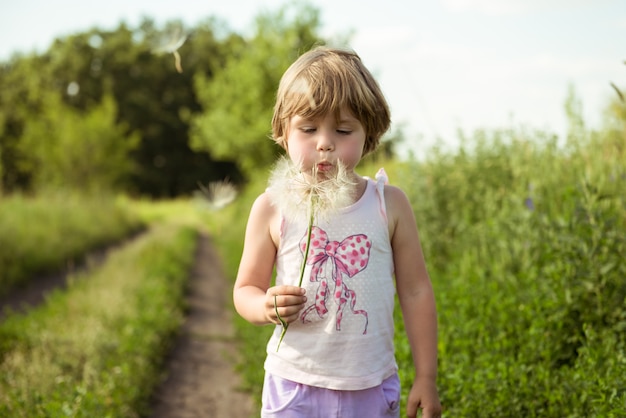 Happy child blowing dandelion outdoors in spring park