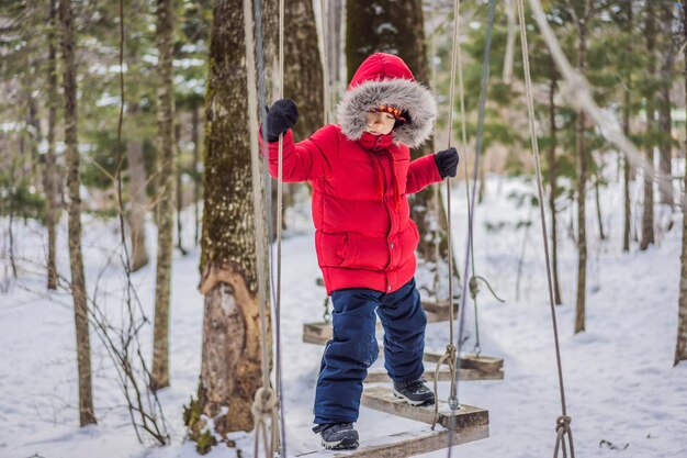 Happy child boy enjoying activity in a climbing adventure park on a winter day