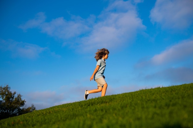 Happy child boy runs around the green field on blue sky, emotional walk on nature and happiness. Cute little boy having fun outdoors.