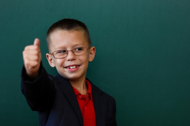 A Happy child child standing at the blackboard with a school backpack wearing glasses