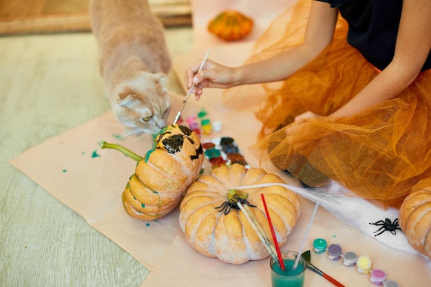 Happy child decorating a pumpkin at home with cat