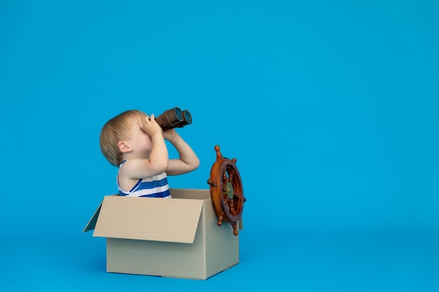 Happy child dreams of becoming a captain against blue wall.