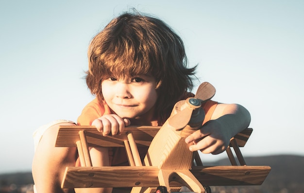 Happy child dreams of traveling and playing with toy airplane Little pilot aviator in outdoor against blue summer sky background Child dreams