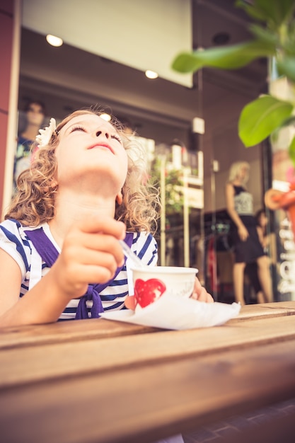 Happy child eating icecream in summer cafe outdoors