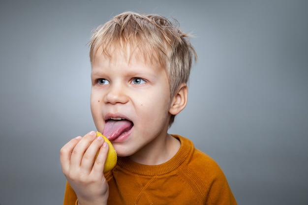 Happy child eating lemon in gray studio