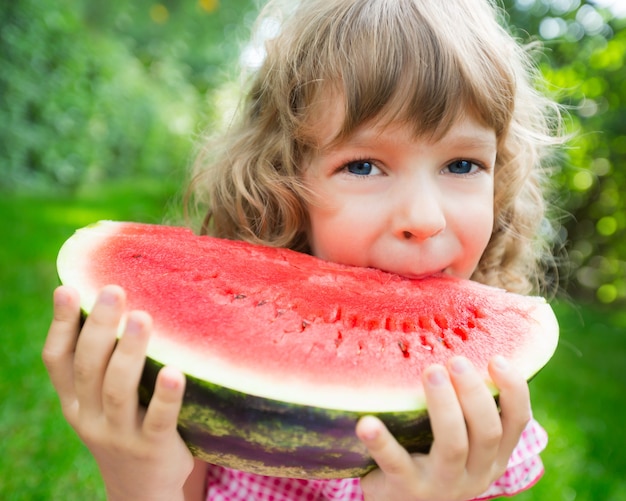 Happy child eating watermelon outdoors in summer park