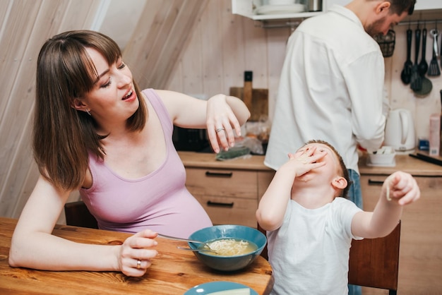 Happy child eats pasta in the kitchen with her family